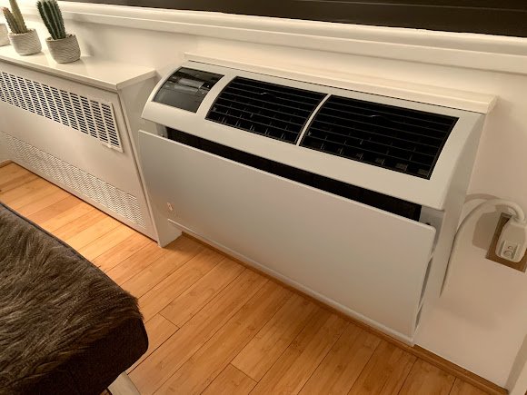 Console-style indoor air conditioning unit mounted near the floor, providing heating and cooling in a modern living space.