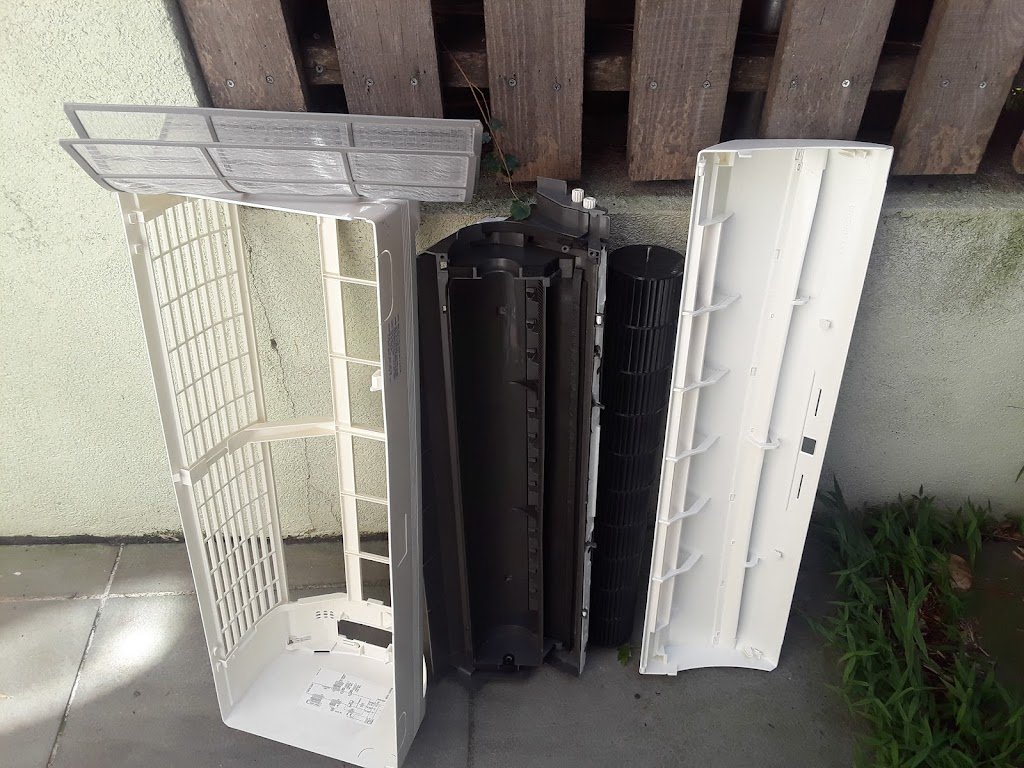 Disassembled indoor split AC unit with its front cover, filter, and blower components removed and laid out for cleaning.